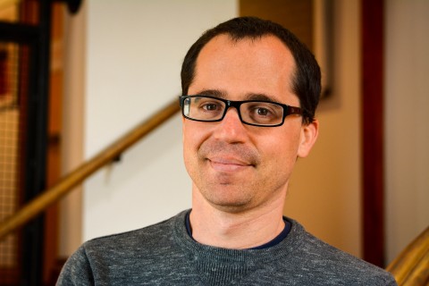 Headshot of Andrew Rosendorf, wearing a black sweater, glasses, and smiling on the stairwell of the Playwrights' Center