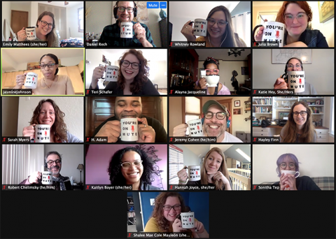 A screen cap of a Zoom meeting. Many staff members are holding coffee mugs next to their face. The mugs have text on them. "You're on Mute"