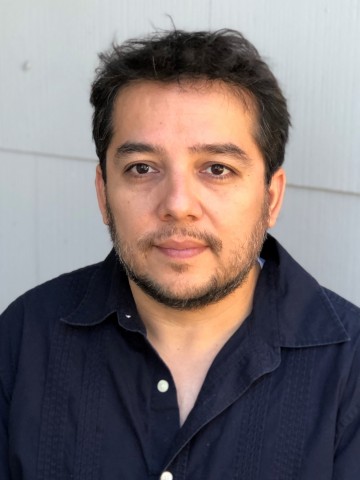 Headshot of Matthew Paul Olmos, a Mexican-American man with short brown hair and stubble, wearing a dark blue shirt