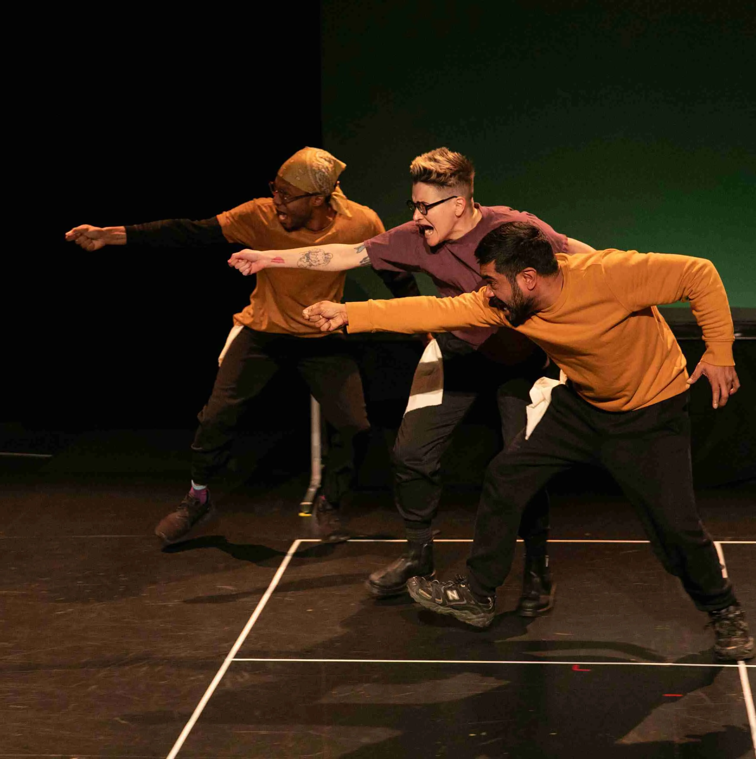 Three actors have imaginary swords drawn and pointed towards someone off stage.